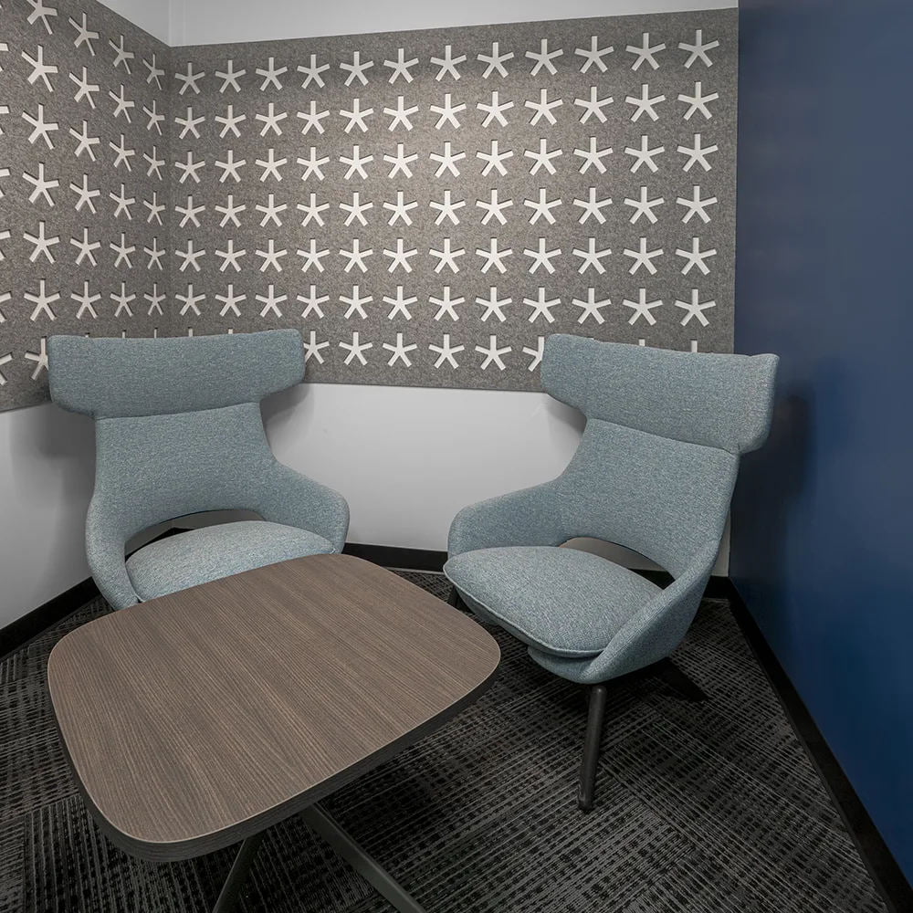 Light grey acoustic wall panel with white stars in office alcove above two blue chairs and brown coffee table