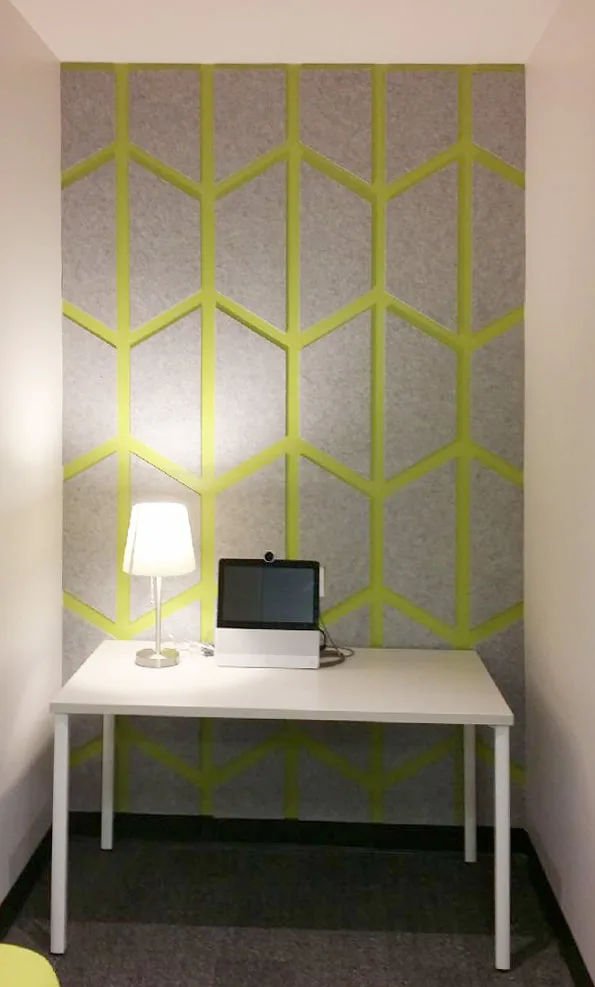 Yellow and grey patterned acoustic wall panel in alcove behind white desk, laptop and white lamp
